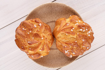Group of two whole fresh baked profiterole on ceramic plate on white wood