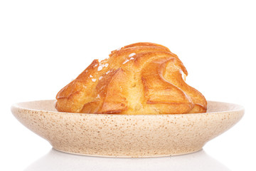 One whole fresh baked profiterole on ceramic plate isolated on white