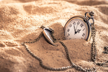 an old pocket watch with a chain lying in the sand - Powered by Adobe