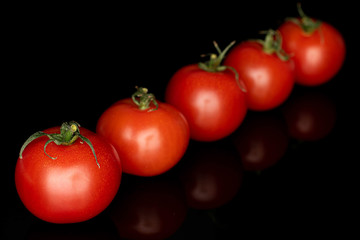 Group of five whole fresh red cherry tomato in row isolated on black glass