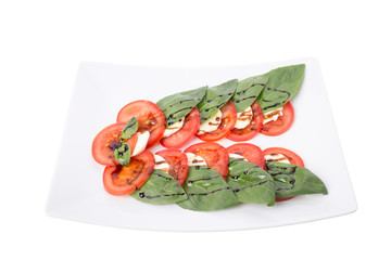 Tomato and mozzarella with basil leaves on a plate.
