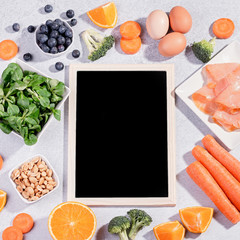 Foods that help maintain eyes healthy, products for keeping good vision, vitamins for eyes. Black board with copy space, assortment of food for eye health on concrete background, flat lay, top view