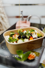 Salad rich in vitamins with olives, feta, zucchini and aubergine in eco box delivered by a delivery service, ordered online, decorated with mint and spices on a retro metal tablet