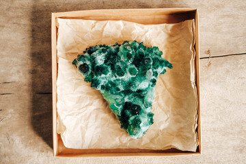 Raw emerald and gemstone rough rock crystal in a kraft paper box on wooden background. Top view....