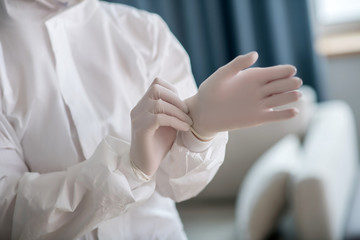 Person in white workwear wearing protective gloves before disinfection