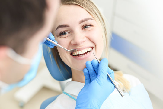 Blond female sits in dentist chair and undergo dentist checkup. Selective focus