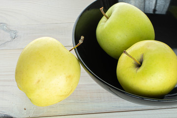 Group of three whole green delicious apple in bowl on white wood