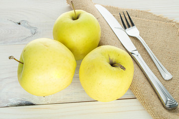 Group of three whole green delicious apple with cutlery on linen on white wood