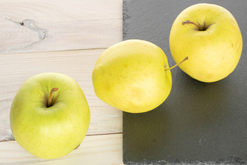 Group of three whole green delicious apple on stone and on white wood