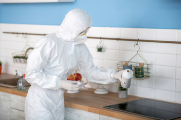 Woman in white workwear and gloves disinfecting the kitchen