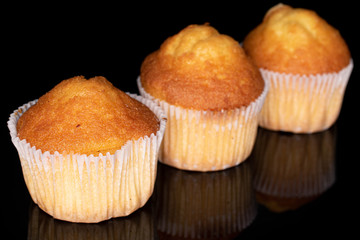 Group of three whole small baked muffin in row isolated on black glass