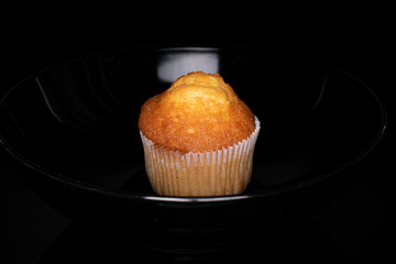One whole small baked muffin isolated on black glass