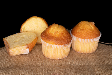 Group of two whole two halves of small baked muffin on jute cloth isolated on black glass