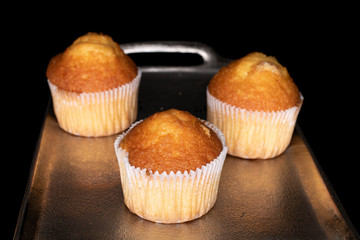 Group of three whole small baked muffin on tray isolated on black glass