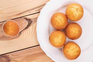 Group of six whole small baked muffin on porcelain plate on wood