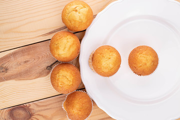Group of six whole small baked muffin on porcelain plate on wood