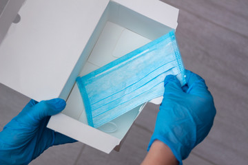 Hands wearing blue medical latex gloves hold an empty box and the last disposable protective...