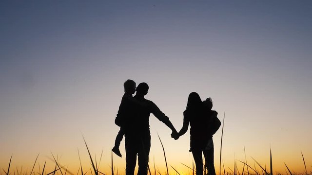 happy family silhouette walking at sunset teamwork. Mom dad daughter and son hold hands go silhouette slow motion video. Happy family lifestyle man girl and kids teamwork concept