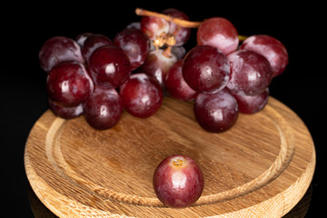 Lot of whole fresh red globe grape on wooden plate isolated on black glass
