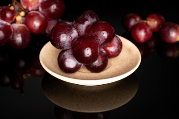 Lot of whole fresh red globe grape on ceramic plate isolated on black glass