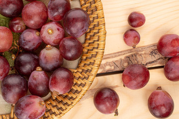 Lot of whole fresh red globe grape on plate with braided edge on wood