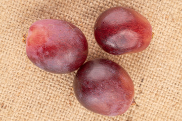 Group of three whole fresh red globe grape berry on tan linen