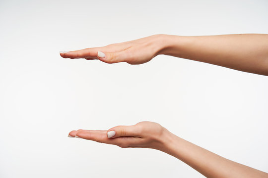 Studio photo of young pretty lady's hands with white manicure measuring invisible items with palms while posing over white background. Human body language concept