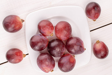 Lot of whole fresh red globe grape on porcelain plate on white wood