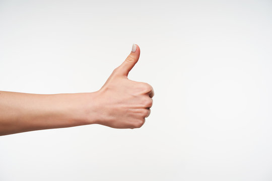 Cropped photo of young woman with white manicure raising hand while thumbing up, showing positive emotions while posing against white background