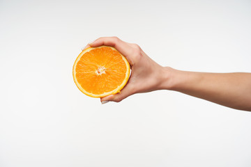 Side view of half of fresh orange being held by young woman's hand while posing over against white...
