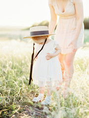 Young mother and baby girl in sunlight at sunset on nature outdoors. Mother and child in meadow in early summer. Photo of natural parenting, dreams, family values, sustainable lifestyle.