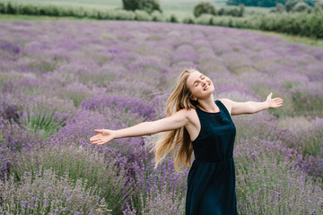 Beautiful woman funny walk on the lavender field on sunset. Beautiful girl in dress stand and flying long hair on purple lavender field. Soft focus. Enjoy the floral glade, summer nature. Hairstyle.