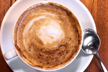 Cappuccino in a white cup on a plate with a spoon. Close up. Top view
