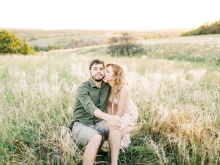 Naklejka na ściany i meble Young couple in love outdoor. Stunning sensual outdoor portrait of young stylish fashion couple posing in summer in field. Film photography. Pretty family hugging and flirting in an park