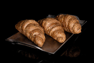 Group of three whole baked wholegrain croissant on tray isolated on black glass