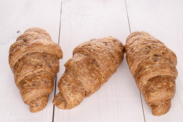 Group of three whole baked wholegrain croissant on white wood