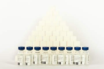 Sugar addiction, insulin resistance, unhealthy diet, sugar cubes pyramid, bottles of insulin for vaccination on white background, diabetes protection medical concept.