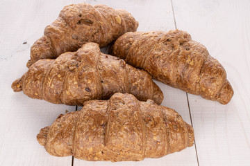 Group of five whole baked wholegrain croissant on white wood