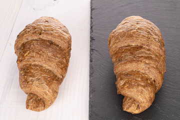 Group of two whole baked wholegrain croissant on stone and on white wood