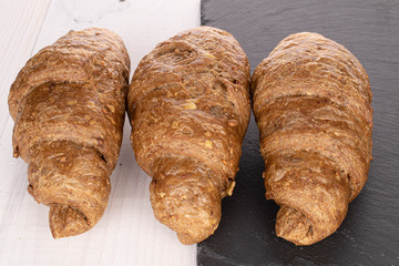 Group of three whole baked wholegrain croissant on stone and on white wood
