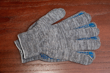 Paired work gloves of gray color on a wooden surface, top view.