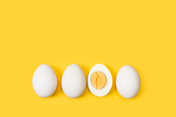 Huevos blancos enteros y uno por la mitad sobre fondo liso amarillo aislado. Vista superior. Copy space - obrazy, fototapety, plakaty