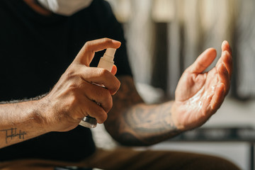 Coronavirus. Man wearing in medical protective mask cleaning hands with sanitizer spray in house to prevent Coronavirus, Covid-19, flu. Spray bottle. Virus and illness protection.