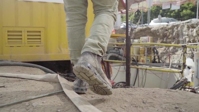 Man walking through working industrial site. Follow shot to a male worker feet in boots. engineering Legs of young man stepping on hose and cables Low angle view Close up Slow motion