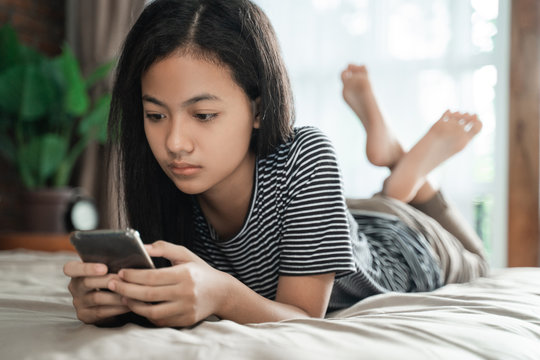 teenager using mobile smart phone at home while laying on the bed