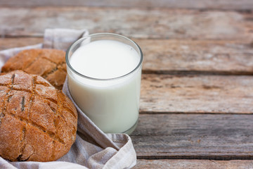 Glass of fresh milk and round brown rye flatbread on a rustic wooden table. Vegetable milk, vegan milk, Kefir, or Turkish Ayran drink for helthy eating. Space for text