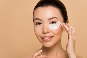 beautiful smiling asian girl with collagen eye pads isolated on beige