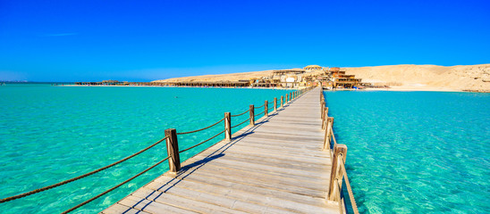 Wooden Pier at Orange Bay Beach with crystal clear azure water and white beach - paradise coastline of Giftun island, Mahmya, Hurghada, Red Sea, Egypt. - obrazy, fototapety, plakaty