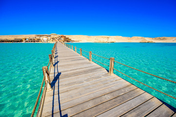 Fototapeta na wymiar Wooden Pier at Orange Bay Beach with crystal clear azure water and white beach - paradise coastline of Giftun island, Mahmya, Hurghada, Red Sea, Egypt.