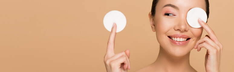 panoramic shot of smiling asian girl removing makeup from face with cotton pads isolated on beige